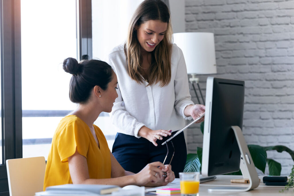 Two young businesswomen reviewing work via digital tablet in the office | ANG