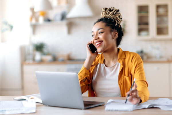 Happy successful busy young african american woman, broker, manager or freelancer working remotely, have pleasantly conversation with client or employee on the phone looking away smiling friendly