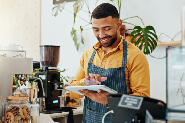 Waiter, smile and tablet in coffee shop for business, online order and delivery service platform. Male barista, tech and software in restaurant for POS, stock management or company information update